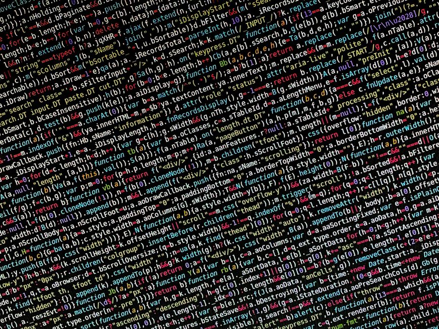 Close-up of a person's hand operating a laptop on a wooden desk, with the screen displaying lines of code in a text editor. The individual is wearing a black wristwatch, and the scene suggests work re